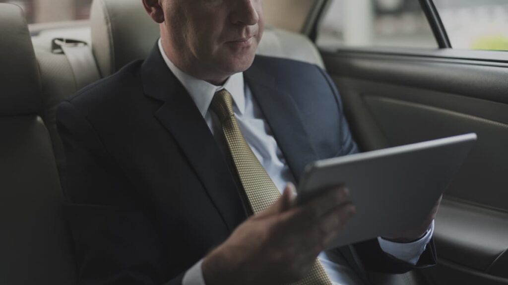 Homme en costume utilisant une tablette sur la banquette arrière d’une voiture.