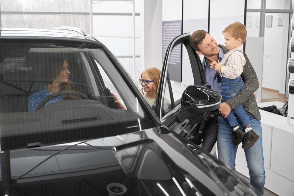 Famille autour d’une voiture dans un hall, avec un homme tenant un enfant dans ses bras.