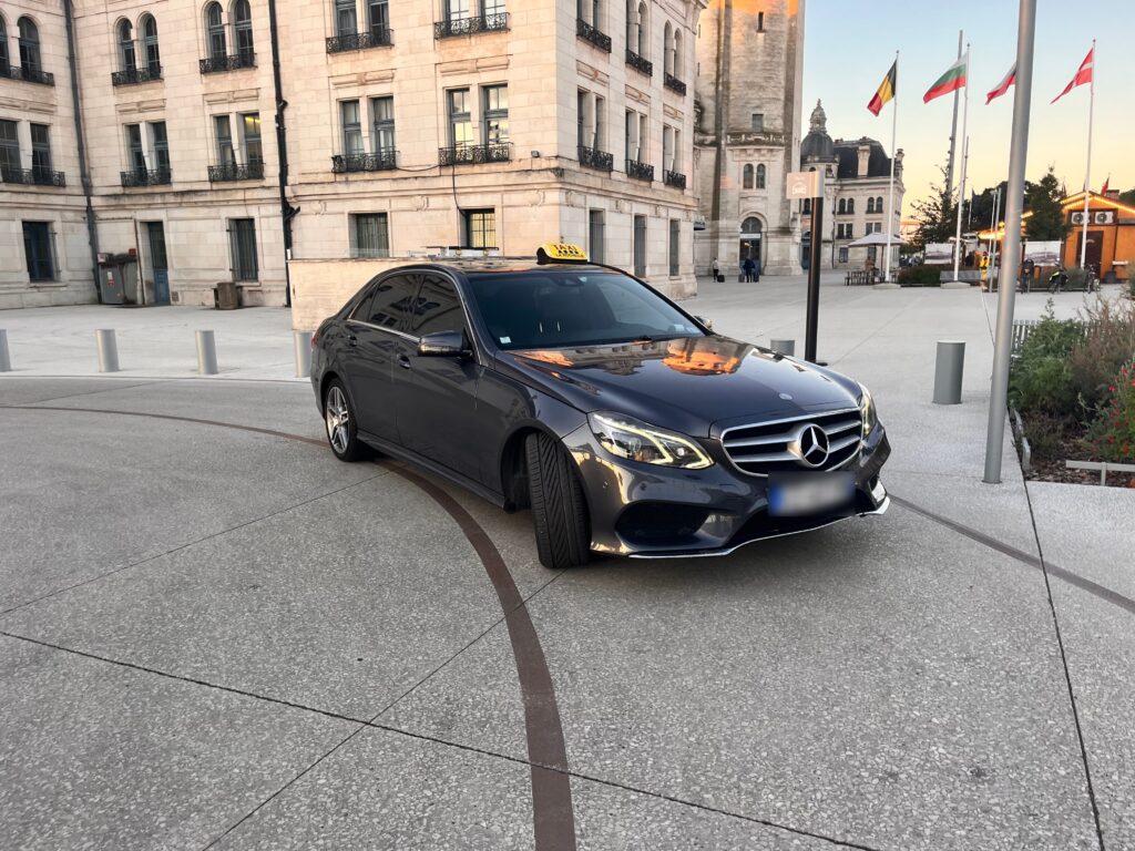 Taxi Mercedes noir stationné sur une place devant un bâtiment en pierre.