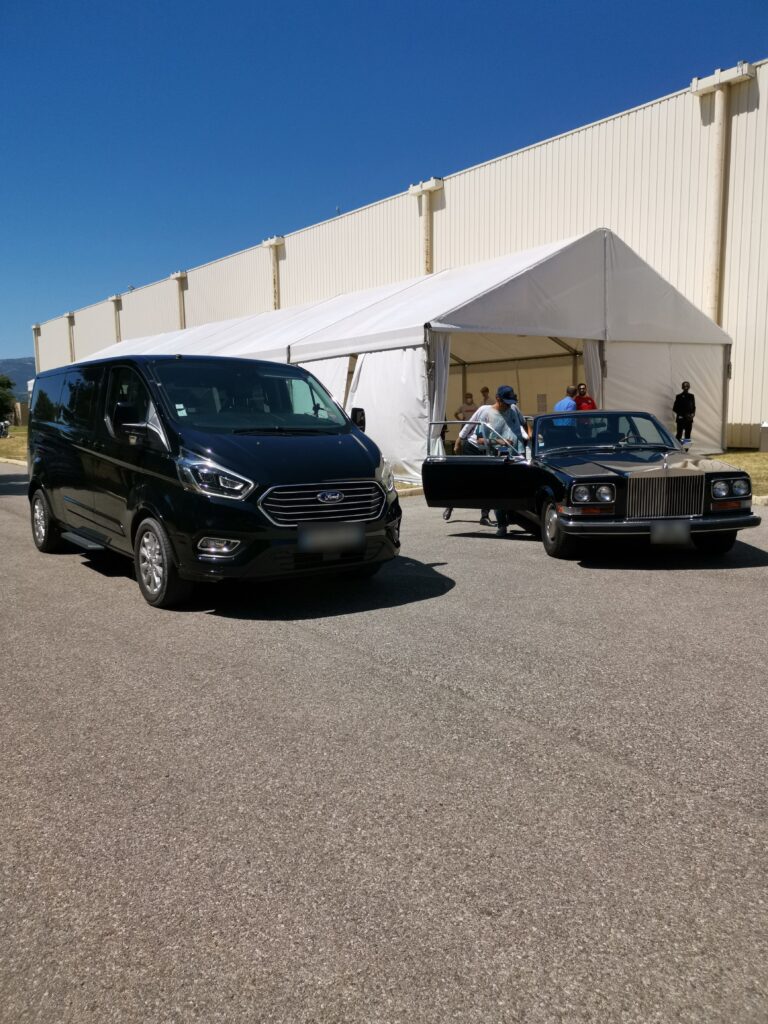 Van Ford noir et voiture de collection stationnés devant un chapiteau blanc.
