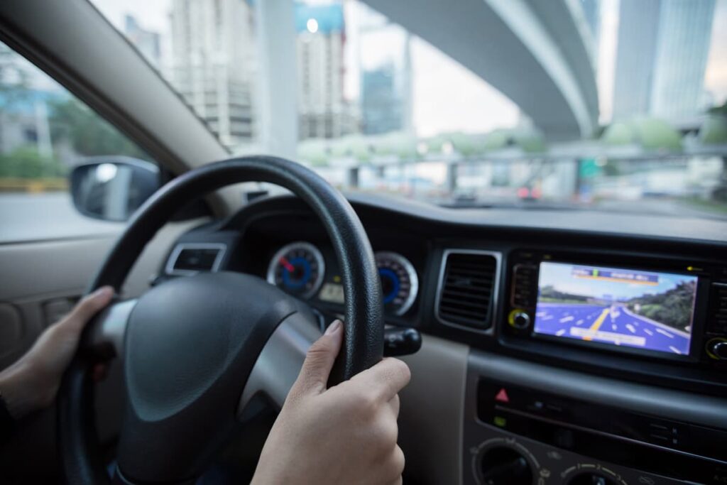 Mains sur le volant d’une voiture avec un GPS affiché au tableau de bord.