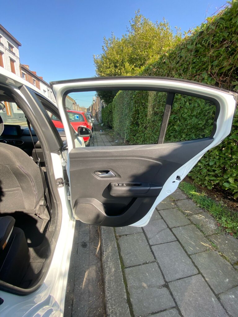 Portière arrière ouverte d’une voiture blanche stationnée le long d’un trottoir.