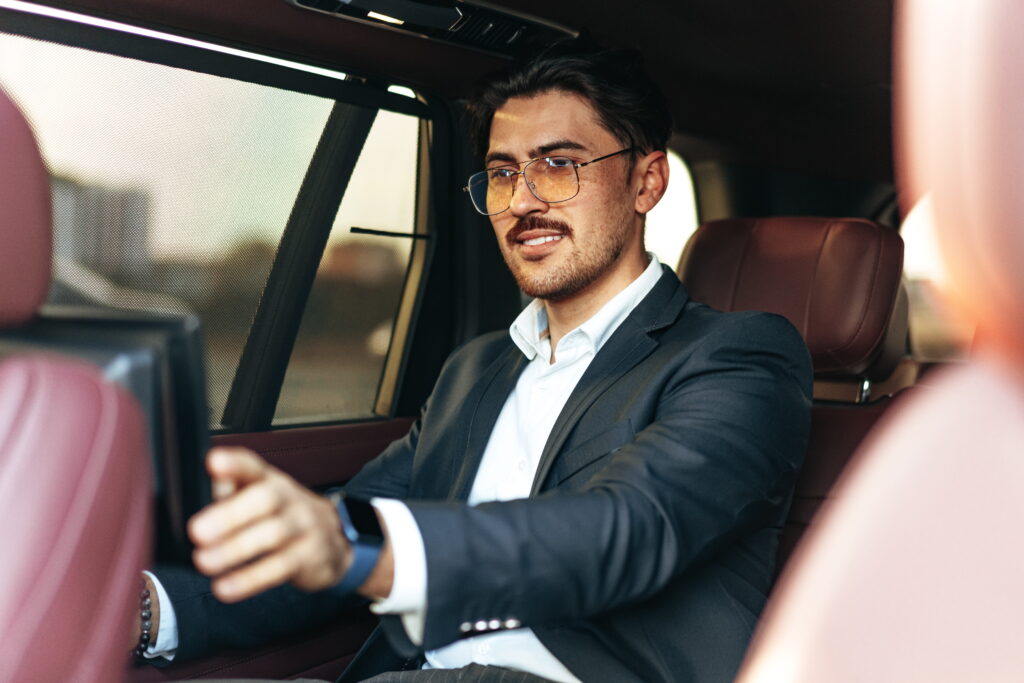 Homme en costume et lunettes assis à l’arrière d’un véhicule avec un ordinateur portable.
