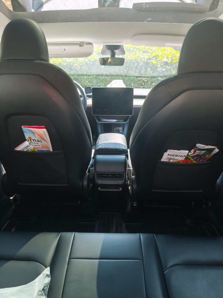 Habitacle d’une voiture vu depuis la banquette arrière, avec des magazines dans les poches des sièges.