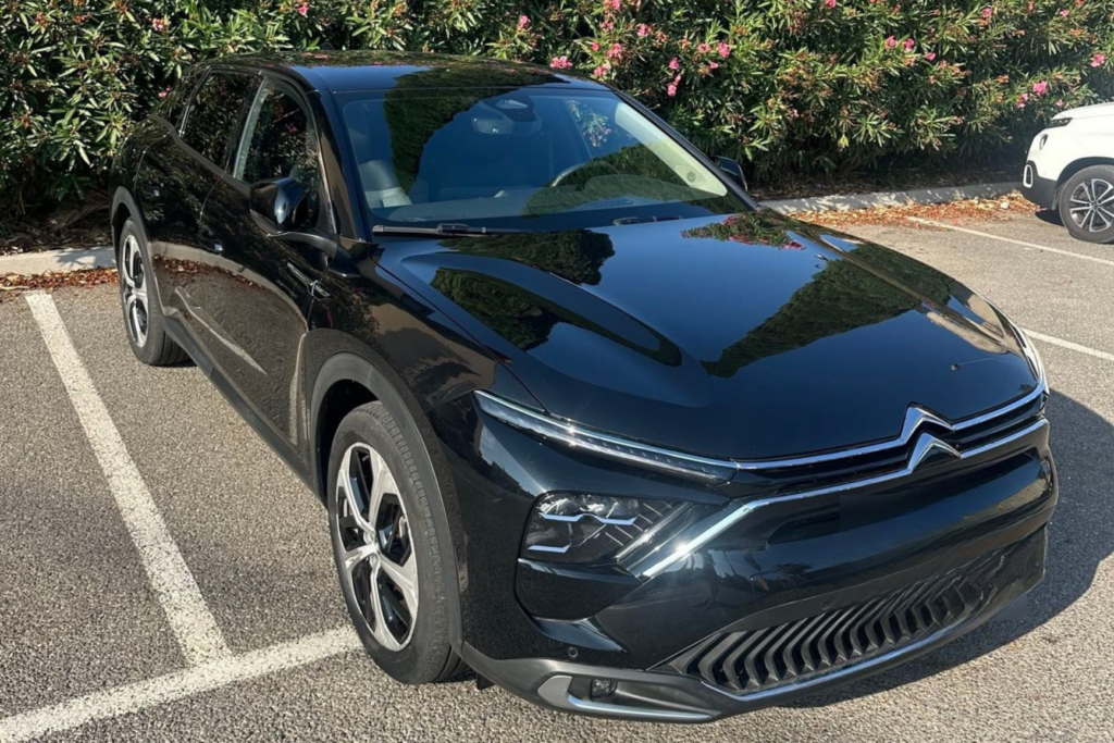Citroën noire stationnée devant une haie fleurie.
