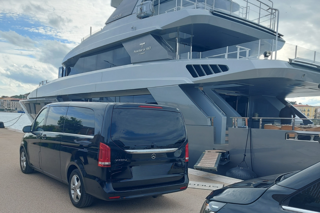 Van Mercedes noir stationné sur un quai à côté d’un grand yacht.