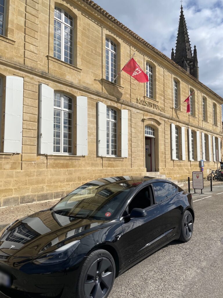 Tesla noire stationnée devant un bâtiment en pierre et un clocher.